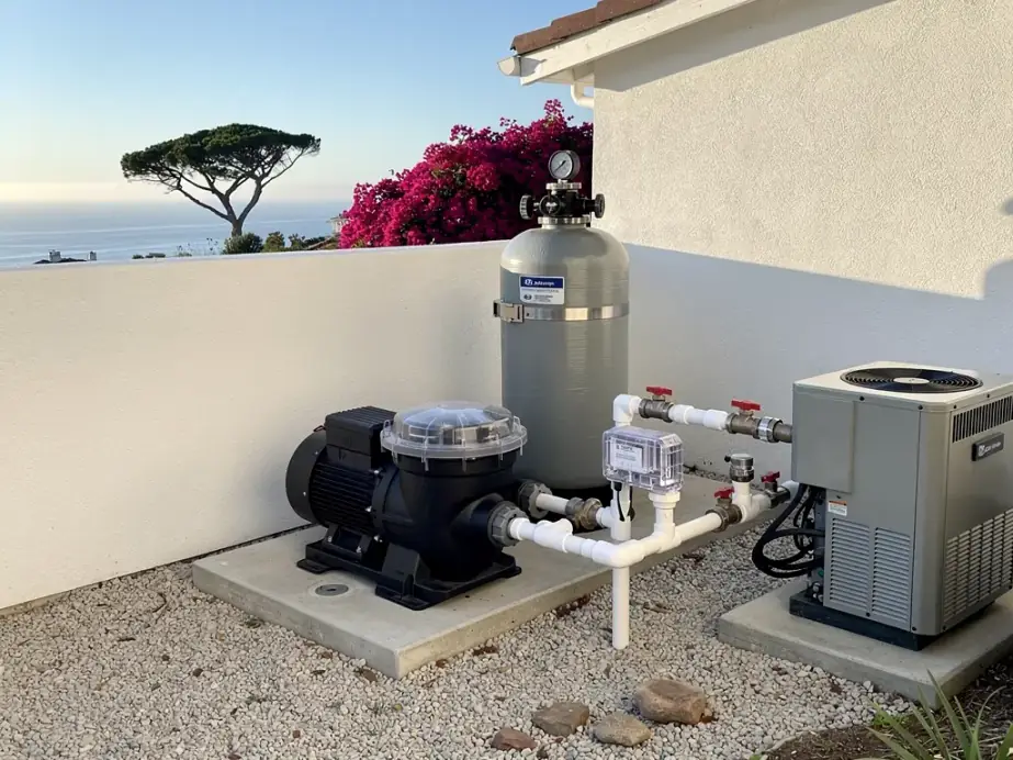 A pool equipment pad against a white stucco wall: pump, D.E. filter tank with gauge, salt cell and valves